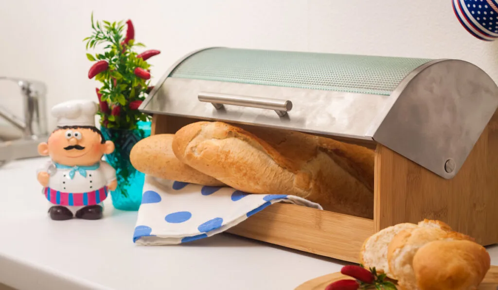 Baguette, lying in a breadbox, made of wood with metal lid
