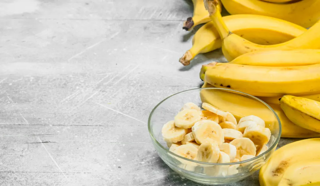 Bananas and banana slices in a glass plate on gray background