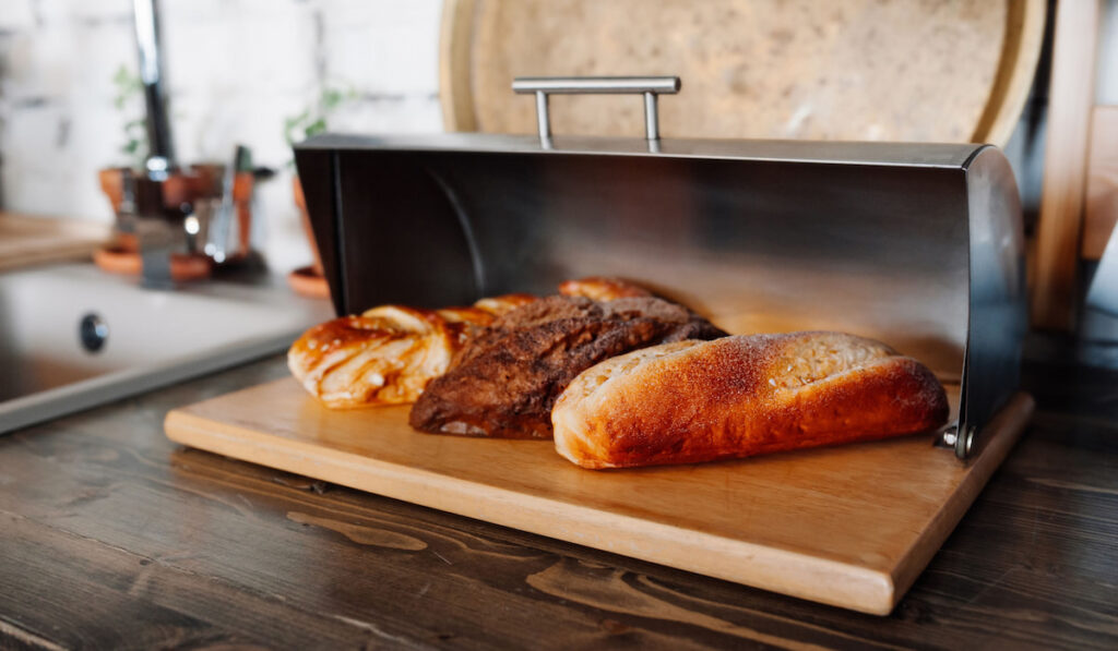 Bread lie in a metal silver breadbox on a wooden table in the kitchen