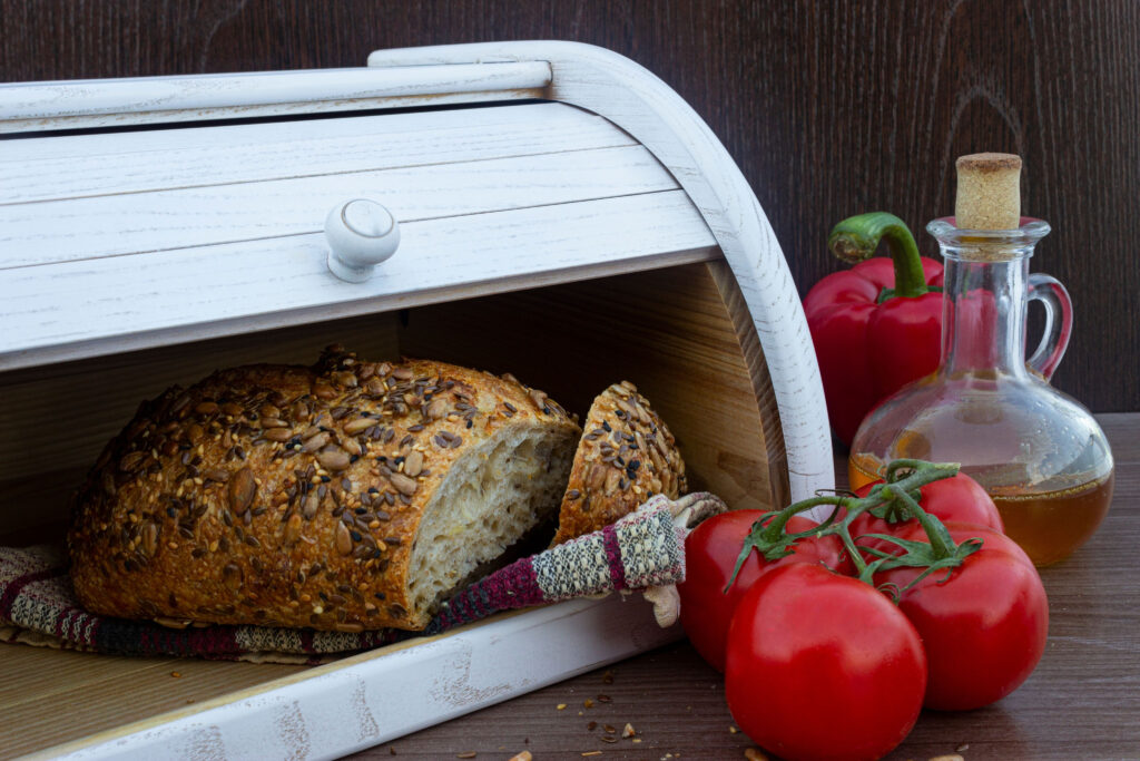 Freshly baked bread with seeds in wooden bread box with tomatoes and olive oil on the table