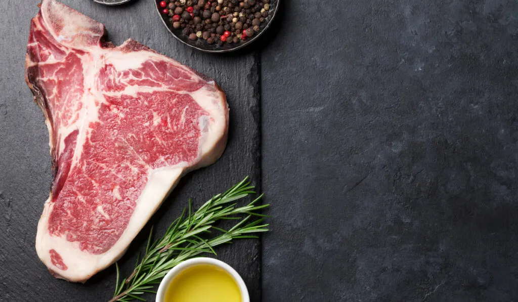 Raw T-Bone beef cut on black stone table with spices on the side