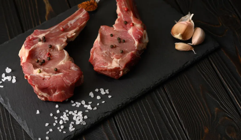 Raw cowboy steak and spices on a black wooden background.
