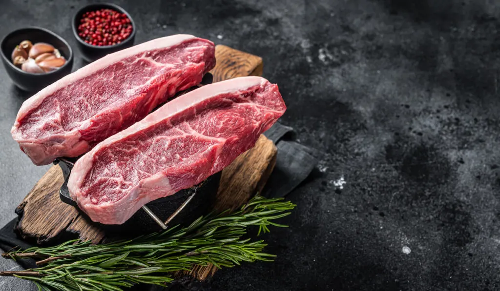 Raw top sirloin beef meat steak on grill on Black background with spices on the sides