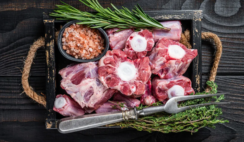 Raw veal beef Oxtail Meat in wooden tray with thyme. Black wooden background.