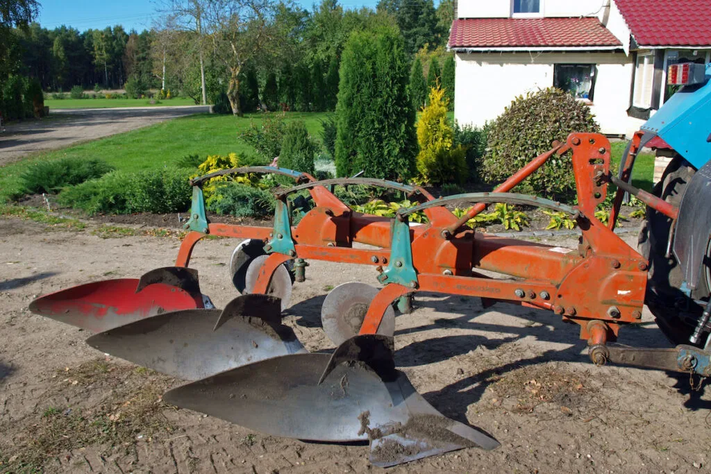 Tractor powered three furrow plow in country yard
