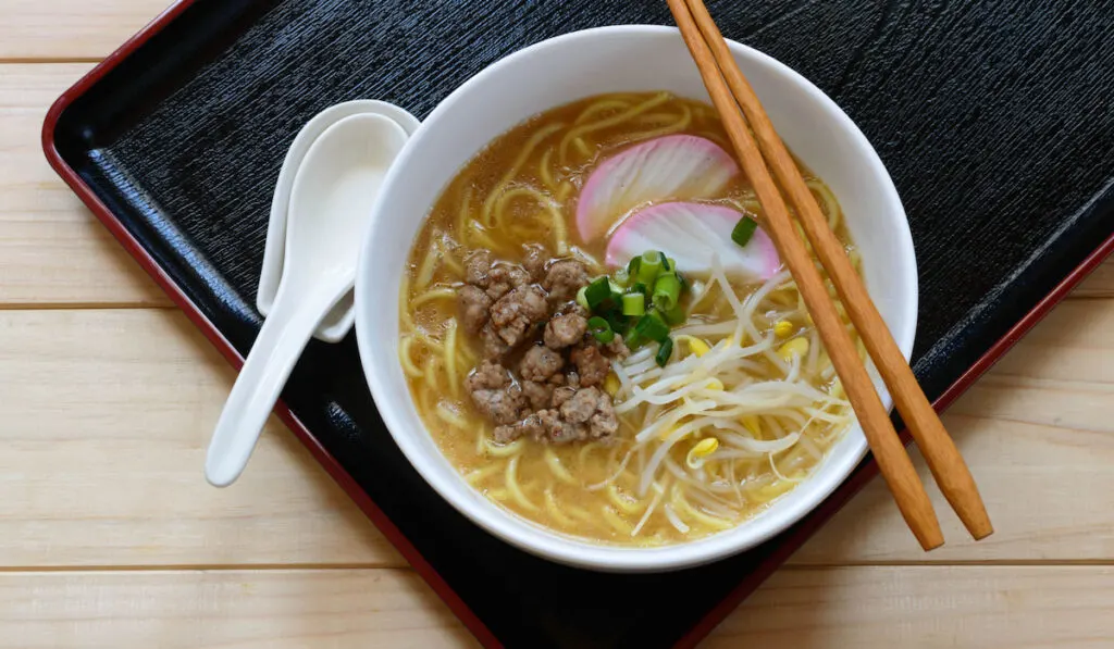 a bowl of gluten free ramen noodles topped with fish cake, ground pork and bean sprouts
