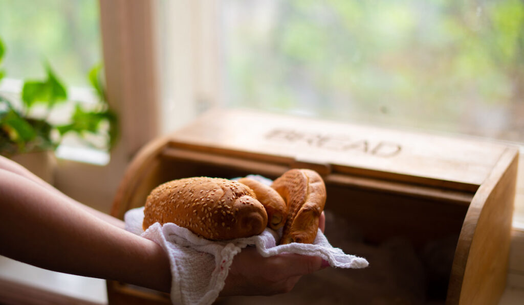 woman taking a bread loaf from a bread box in the kitchen at home
