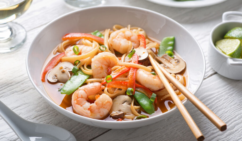 A bowl of spicy asian ramen shrimp noodle soup with mushroom, red pepper, snap peas and scallions