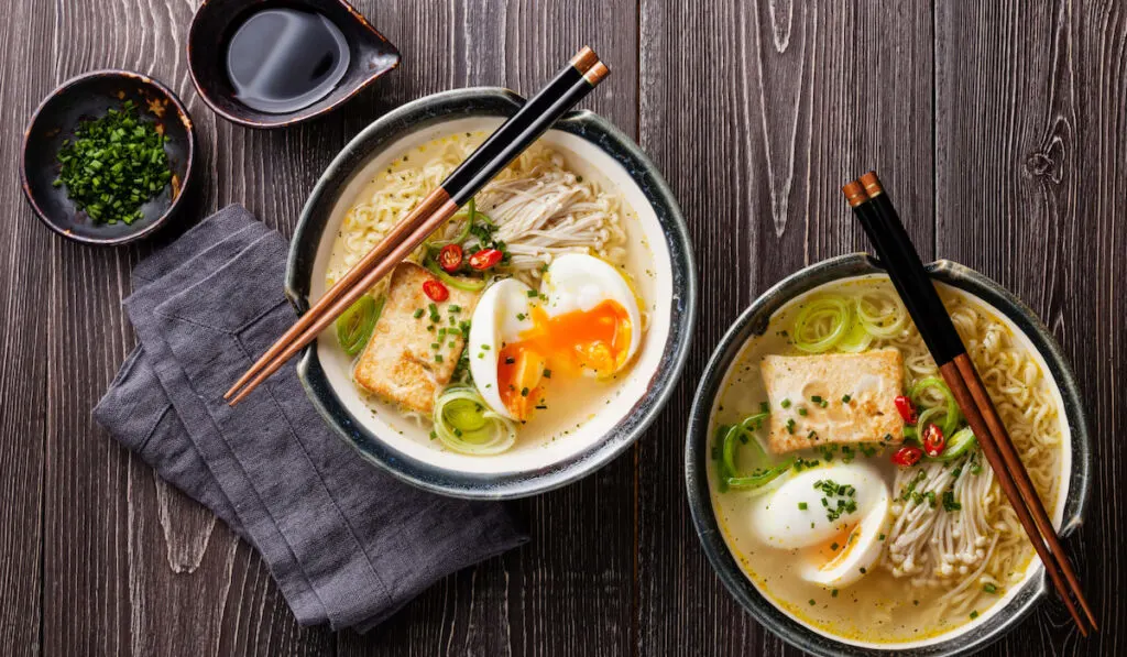 Asian Miso ramen noodles with egg, tofu and enoki mushroom in bowls on brown wooden background