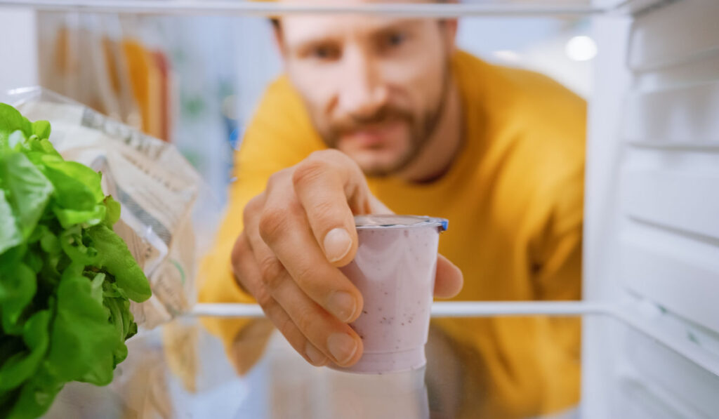 Camera inside fridge, man taking out yogurt 