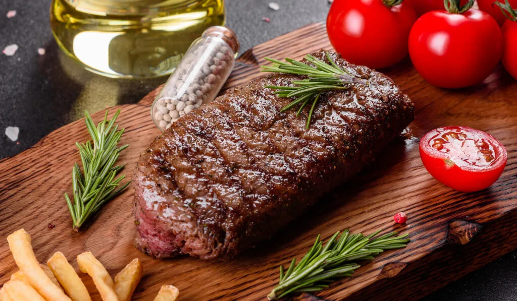 Cooked ribeye steak with potatoes and cherry tomatoes on wooden board