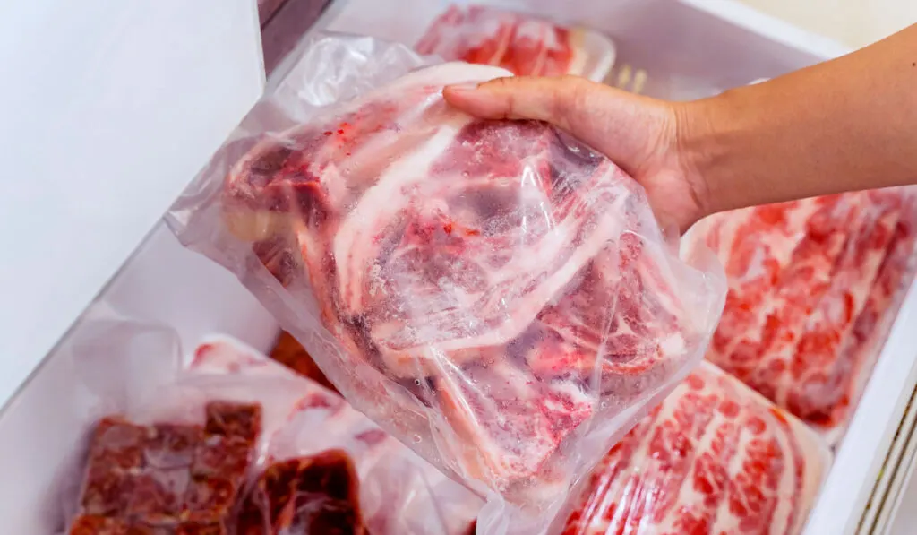 Hand choosing frozen raw meat steaks in plastic in the freezer 