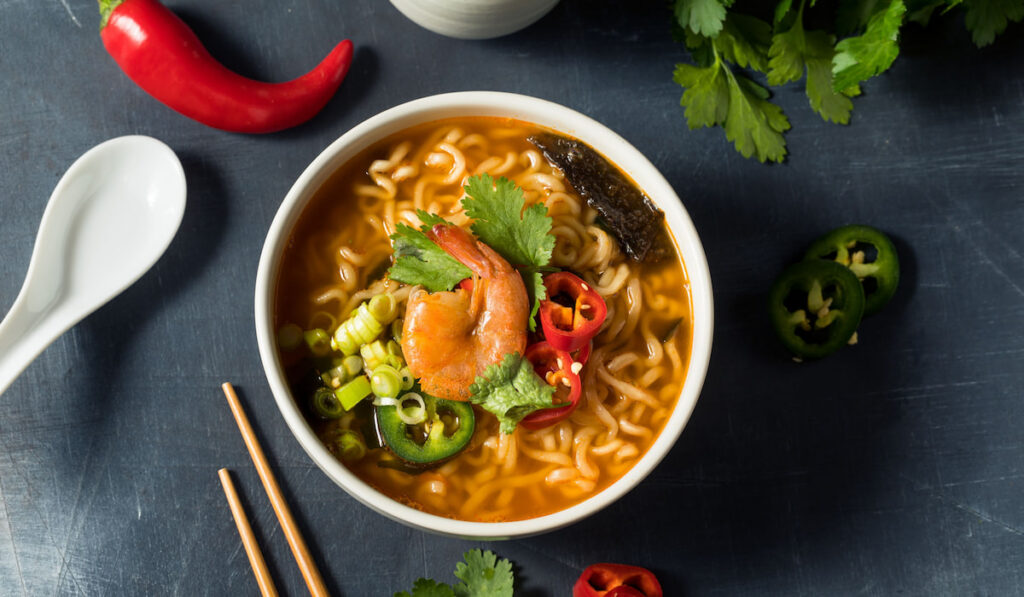 Instant Spicy seafood ramen with shrimp and chili peppers on dark blue background