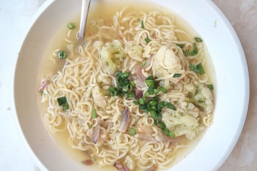 Instant ramen noodle soup with Cauliflower and green onions in white bowl