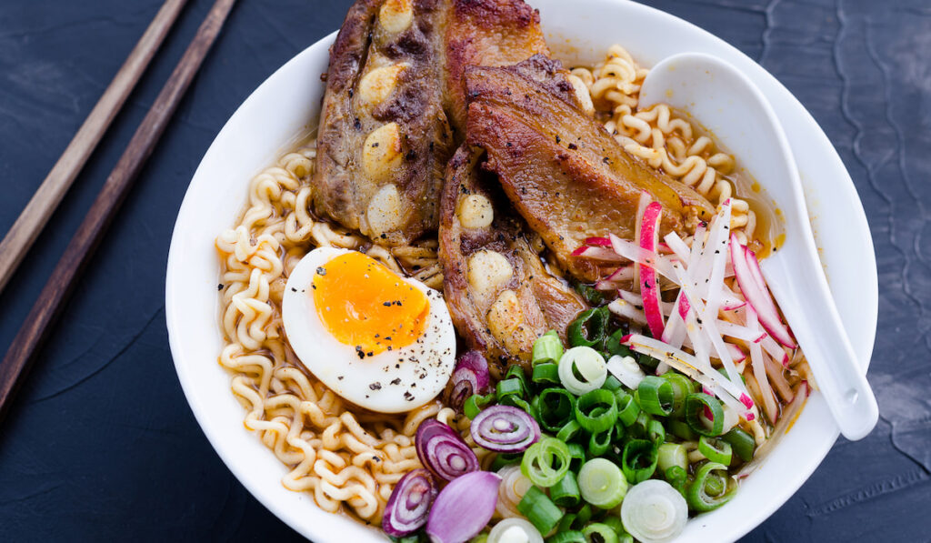 Japanese ramen noodle soup with pork egg and onion on dark blue background