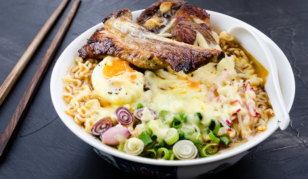 Japanese ramen noodle soup with pork, egg, onion and cheese on dark wooden background