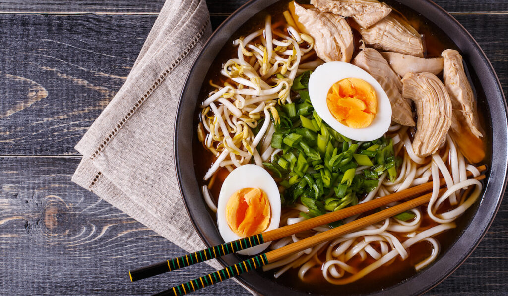 Japanese ramen soup with chicken, egg and bean sprout in black bowl on dark wooden background