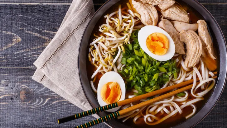Japanese-ramen-soup-with-chicken-egg-and-bean-sprout-in-black-bowl-on-dark-wooden-background