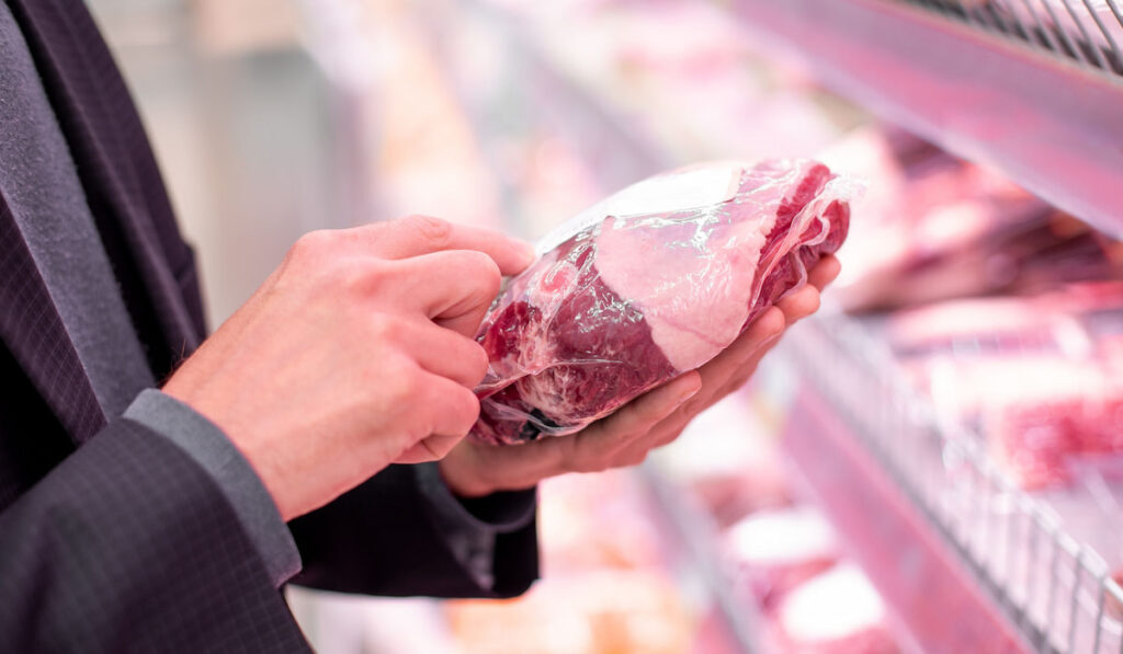 Man reads meat steak information stands near the refrigerator in supermarket