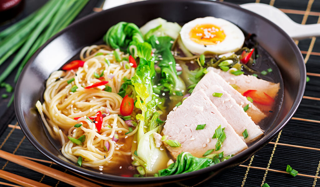 Miso Ramen noodles with egg, pork and pak choi cabbage in black bowl on dark background
