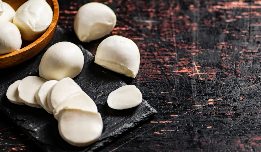 Pieces and slices of mozzarella cheese on a stone board against a dark background