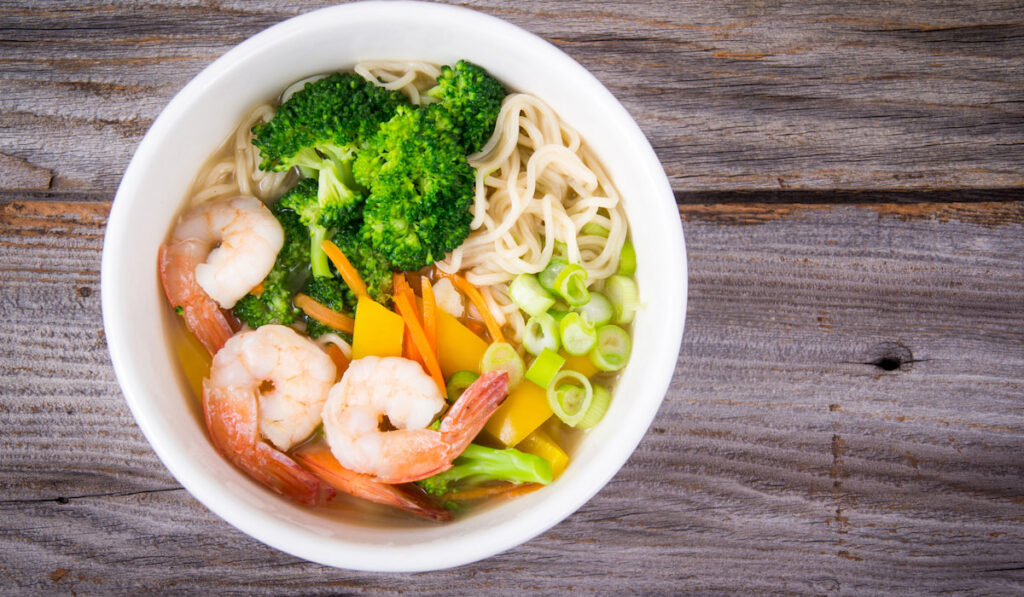 Ramen noodle prawn soup bowl with broccoli and green onion on wooden table