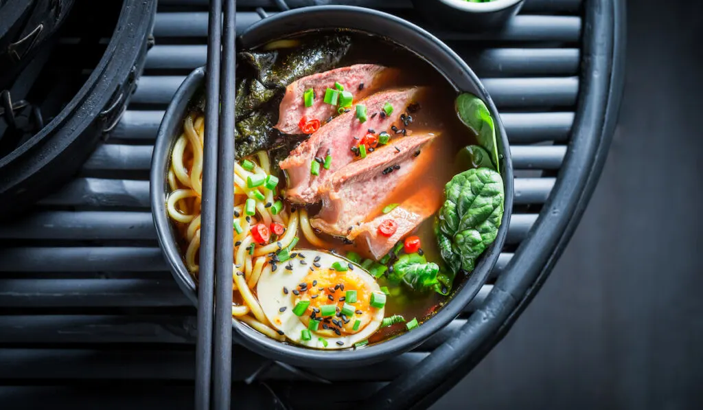 Ramen soup with noodles, egg and spinach in black bowl on black table