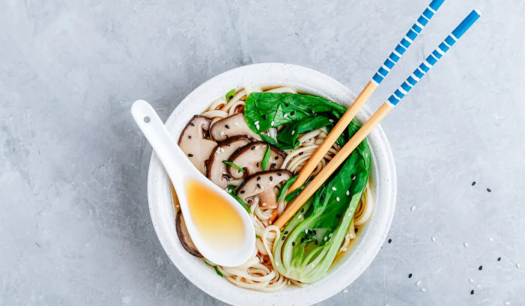 Ramen noodle soup in a bowl with Shiitake mushrooms and bok choy on gray stone background