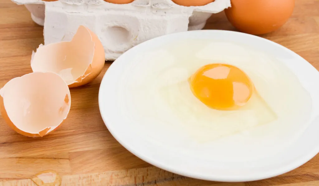 Raw egg on a plate with whole eggs on the table 