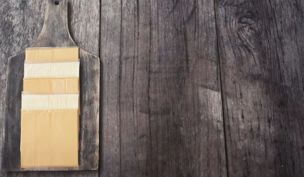 Slices of american cheese on wooden board on wooden background