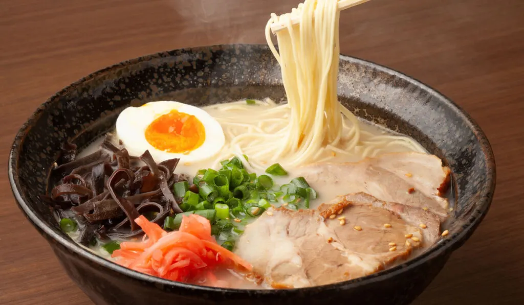 Tonku Ramen in white cheesy pork based soup in dark bowl on wooden table