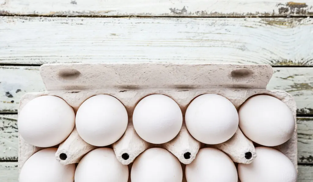 Top view of raw chicken eggs in egg box on white wooden table