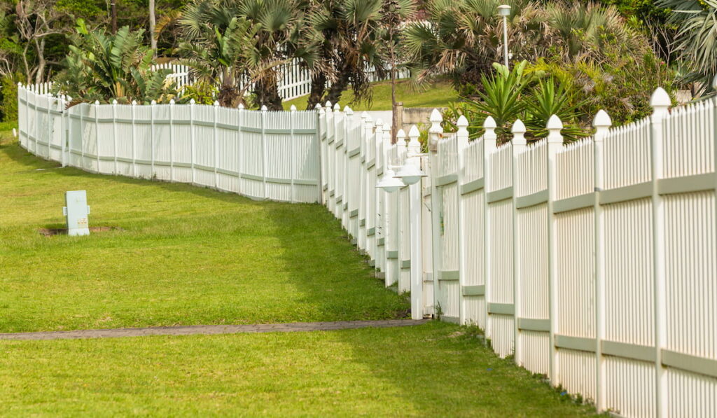White boundary vertical slat plastic pvc fence along roadside grass landscape