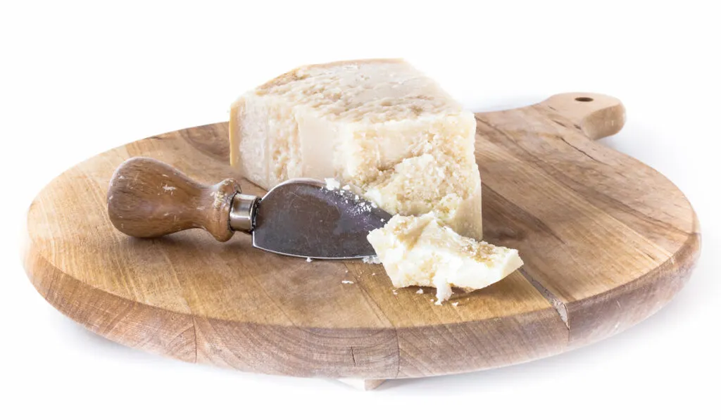 Wooden cutting board with flaked parmesan cheese on white background