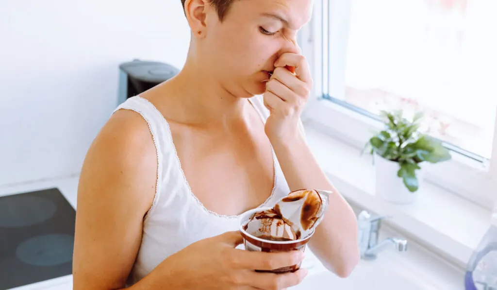 Young girl covering her nose with hand from smelly spoiled yogurt 