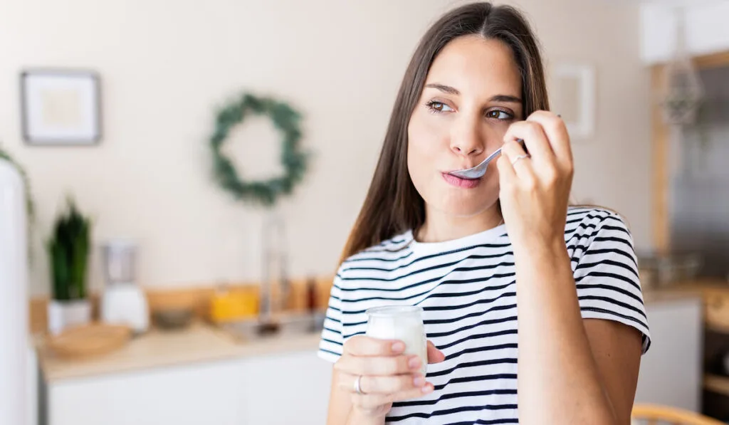 Young woman eating yogurt in the kitchen at home