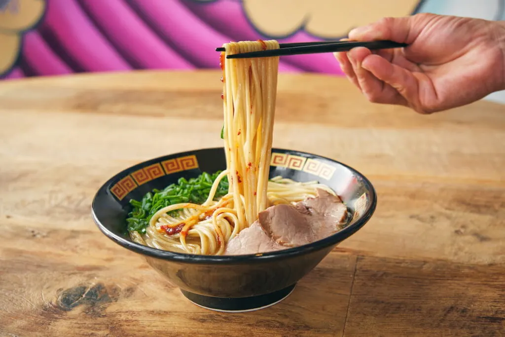 person with noodles on chopsticks above delicious ramen