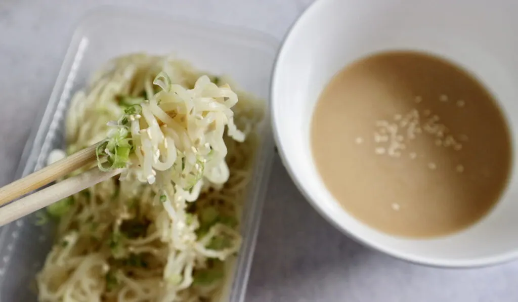 ramen on plastic box and sauce on white bowl