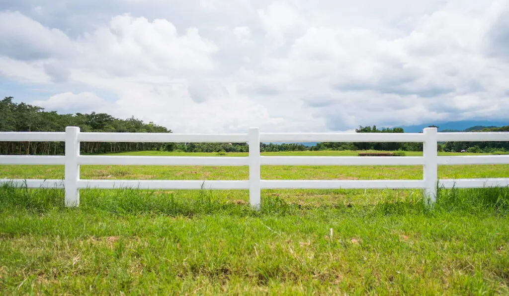 white fence in farm field and overcast sky