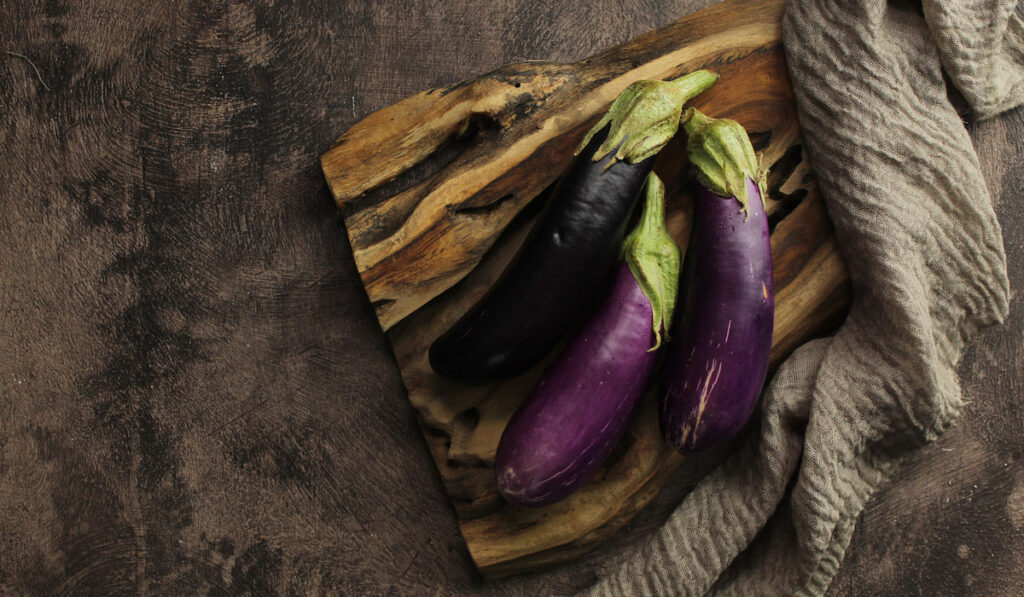 Eggplants on wooden board on dark stone background