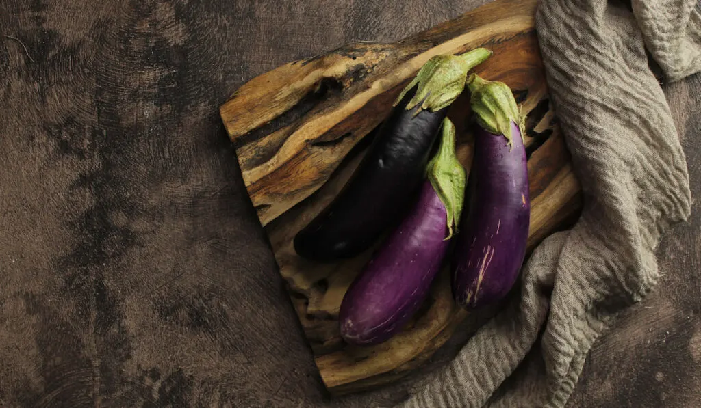 Eggplants on wooden board on dark stone background
