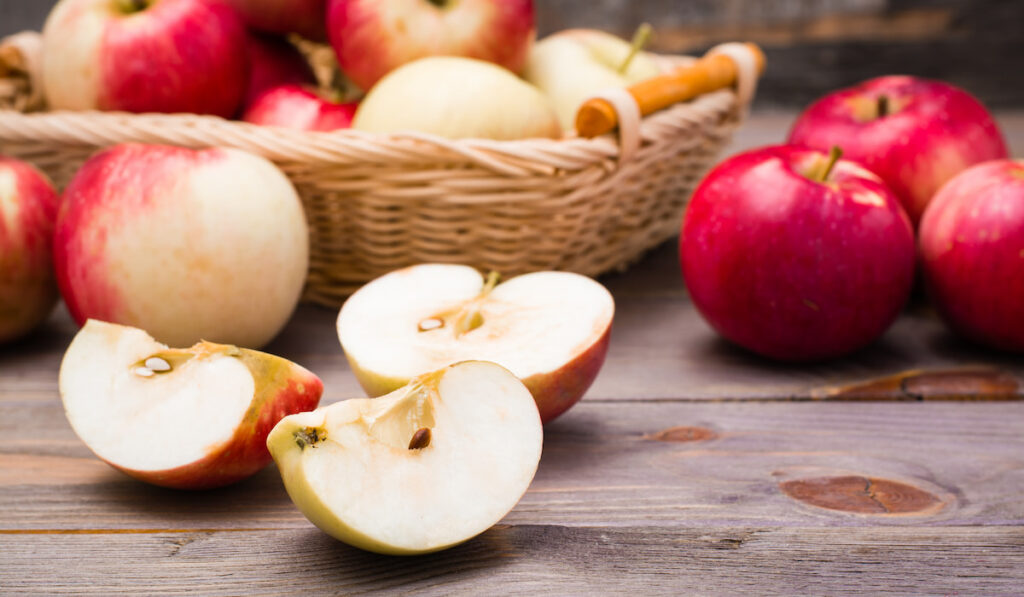 Fresh sliced apple and whole ripe red apples in a basket on a wooden table 