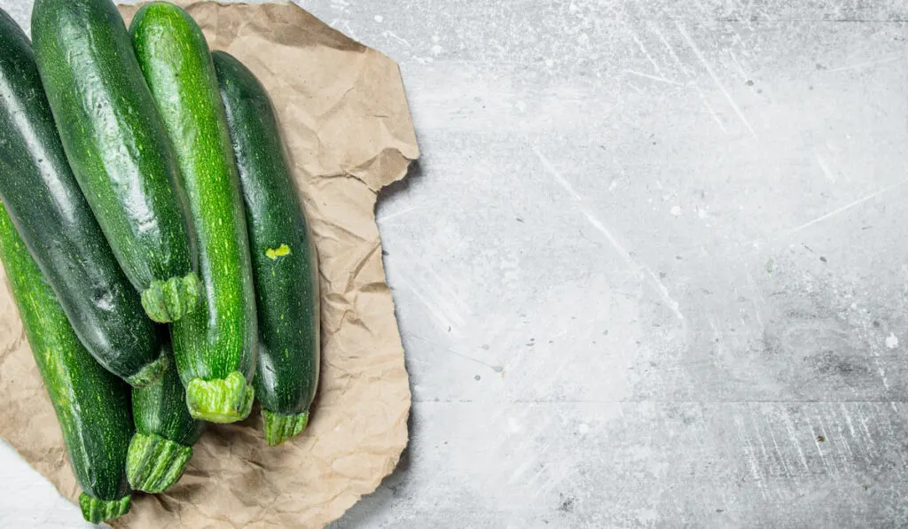 Fresh zucchini on paper on white rustic background