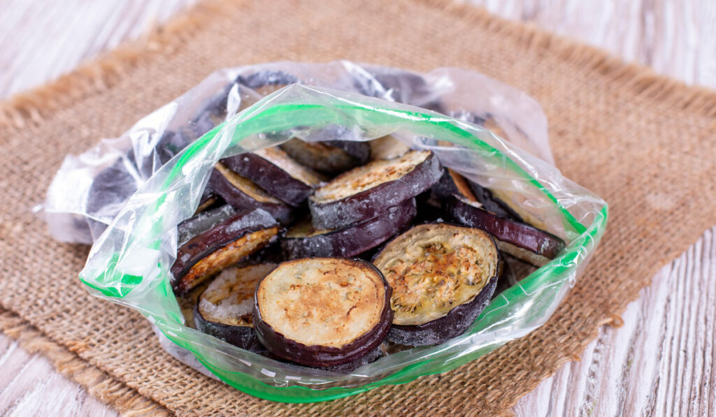 Frozen eggplant in a plastic bag on a wooden table
