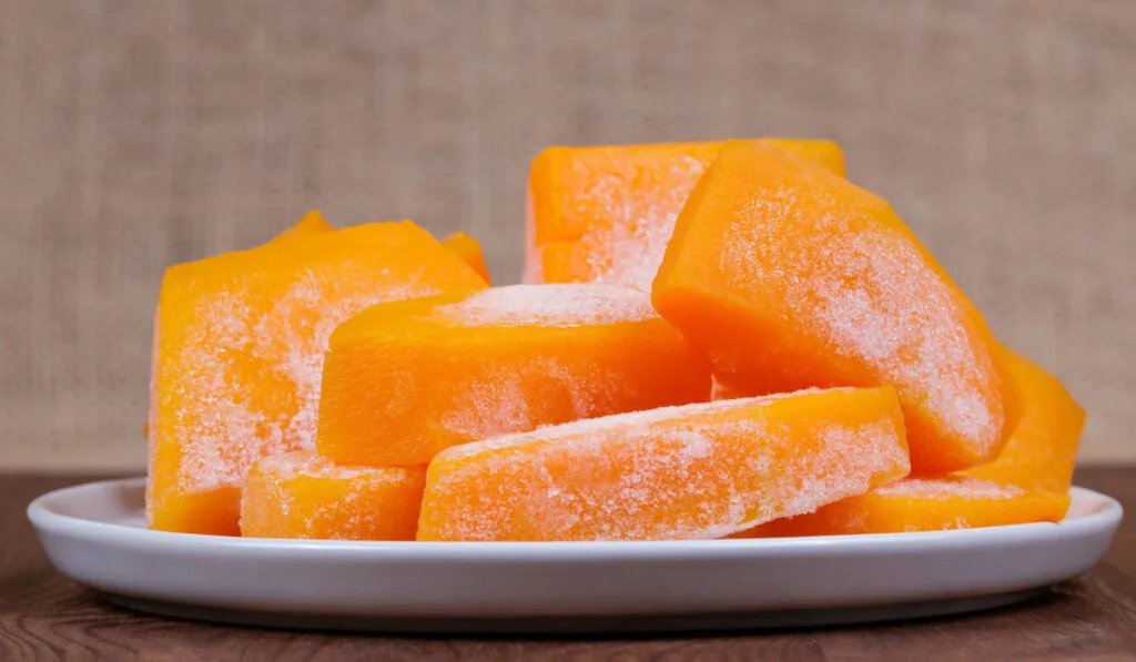 Frozen pieces of squash on the plate on wooden table 