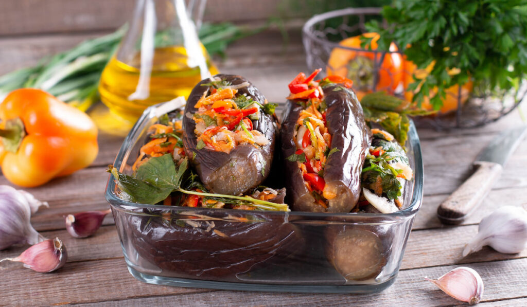 Pickled stuffed eggplant with vegetables in a glass container on a wooden table