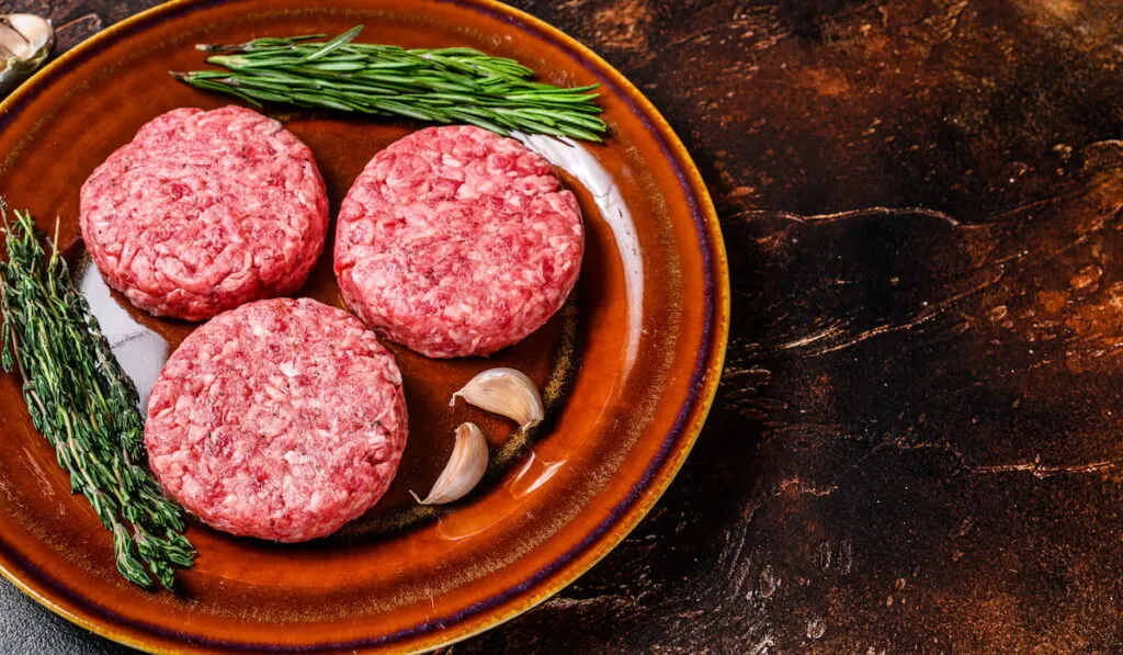 Raw burger meat cutlets with mince beef and herbs on a plate