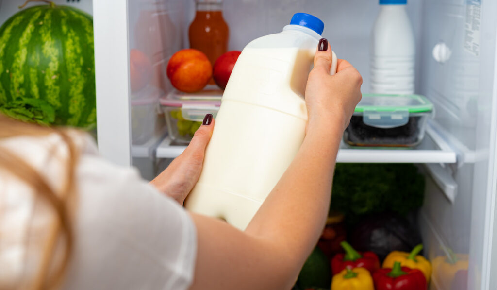 female hand taking bottle of milk from a fridge