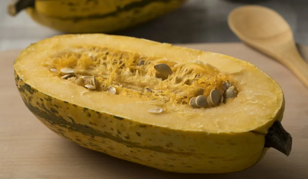halved raw spaghetti squash and seeds on wooden table with wooden spoon