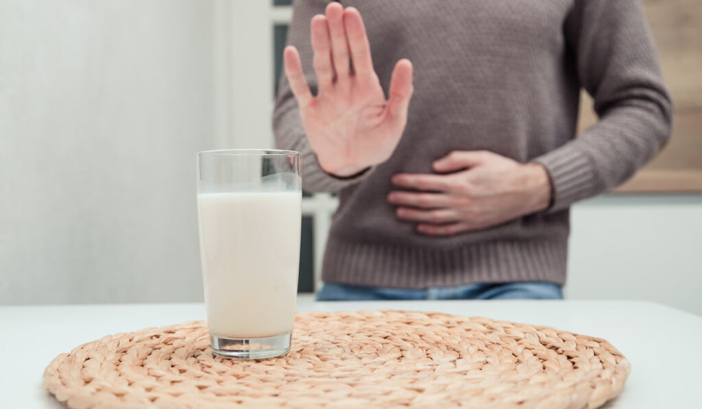 hand of a man showing stop in front of glass of milk on the table, bad milk concept